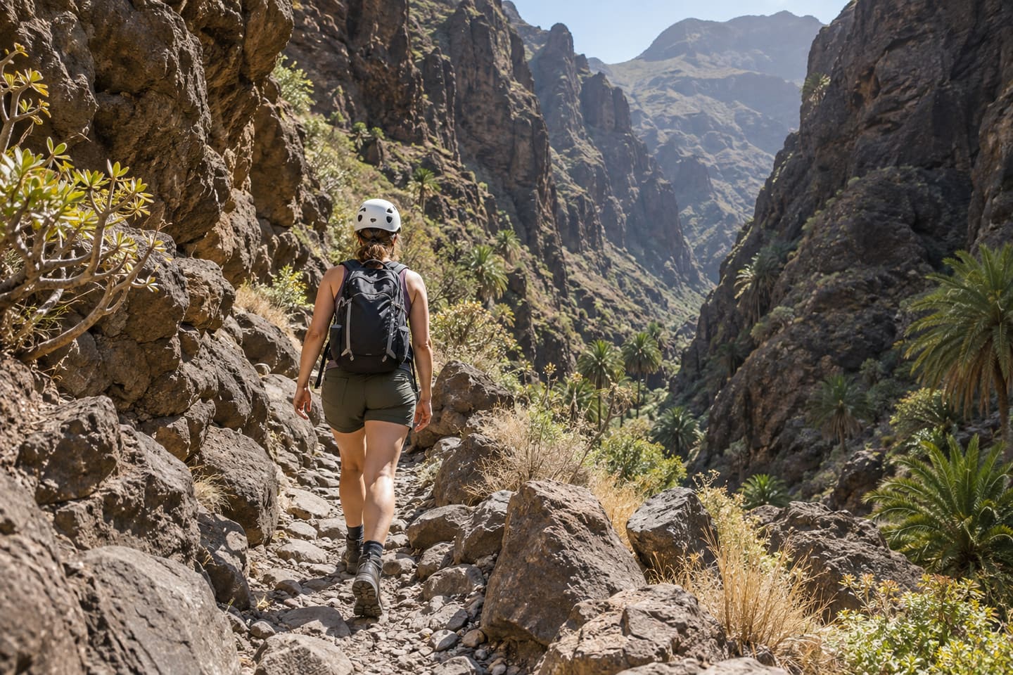 A helmeted hiker in mountain boots walking through the volcanic Masca Gorge