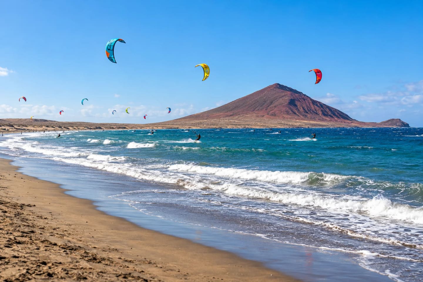 Colourful kites over El Médano bay with the reddish Montaña Roja cone beyond the beach